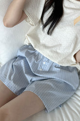 Model sitting on bed in Avauma Sunny Stripe blueberry powder shorts.